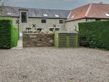 A gravel driveway with a wooden bin enclosure and trimmed hedges in front of a stone building with tiled roof at The Haven in Norham
