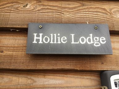 A black sign with white text saying Hollie Lodge mounted on a wooden wall at Hollie in Raglan