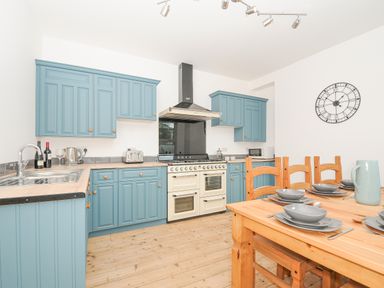 A kitchen with blue cabinets wooden dining table set with dishes and wall clock at Albert House in Looe