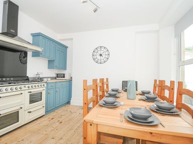 A kitchen with blue cabinets a wood dining table set for six and a large cream oven at Albert House in Looe