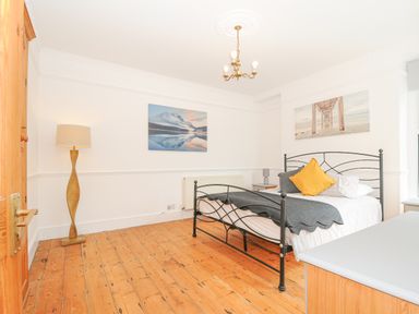 A bedroom with a metal bed frame wooden floor a floor lamp and landscape pictures on the walls at Albert House in Looe