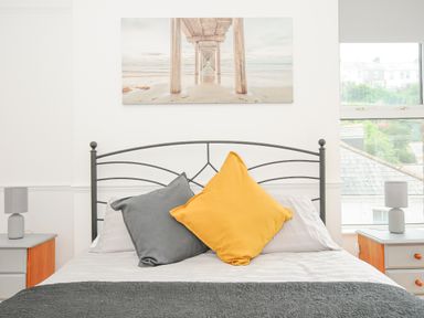 A bedroom with a bed with gray and yellow cushions and nightstands with lamps at Albert House in Looe