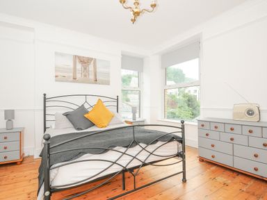 A bedroom with a metal framed bed two gray bedside tables and a gray dresser with a vintage radio at Albert House in Looe