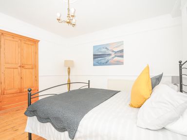 A bedroom with a metal bed frame wooden wardrobe floor lamp and landscape picture on the wall at Albert House in Looe