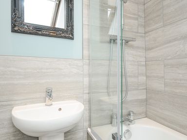 A bathroom with a white sink mirror and shower over bathtub at Albert House in Looe