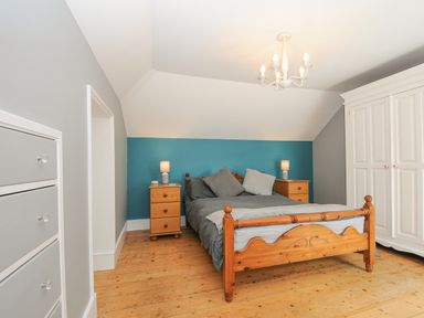 A bedroom with wooden bed frame two bedside tables with lamps a white wardrobe and a chest of drawers at Albert House in Looe