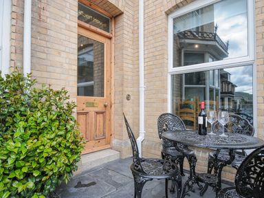 A small outdoor patio with a black metal table and chairs and a bottle of wine in front of a wooden door at Albert House in Looe