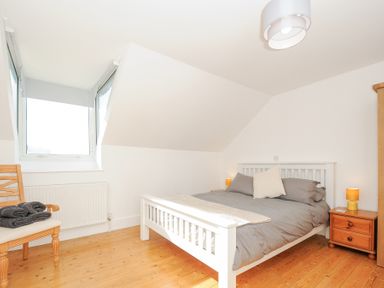 A bedroom with a white bed frame gray bedding a wooden chair with towels a wooden nightstand and a window at Albert House in Looe