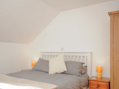 A bedroom with a bed with gray sheets and pillows a white headboard two bedside tables with yellow lamps and a wooden wardrobe at Albert House in Looe