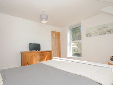 A bedroom with a wooden dresser and a television near a wooden door and a window at Albert House in Looe