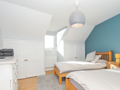 A bedroom with two single wooden beds a blue accent wall a window and a white dresser at Albert House in Looe