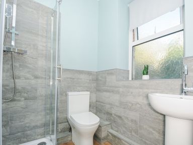 A bathroom with a shower enclosure toilet sink and a frosted window with a small plant on the sill at Albert House in Looe