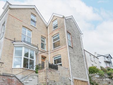 A multi-story brick and stone house with multiple windows and stairs leading to the entrance at Albert House in Looe