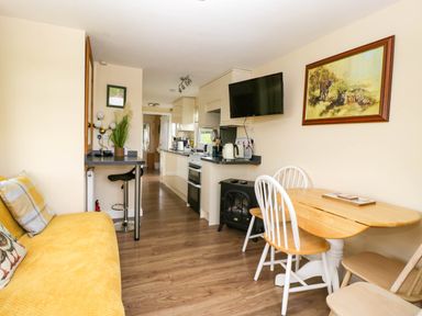 A kitchen area with a wooden table and chairs a sofa and a wall-mounted TV at Poppy in Raglan