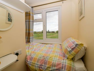 A small bedroom with a single bed next to a window showing a grassy field outside at Poppy in Raglan