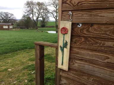 A wooden wall with a painted wooden plaque of a red flower beside a wooden railing with green grass and trees in the background at Poppy in Raglan