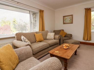A living room with beige sofas yellow curtains a wooden coffee table and a framed map on the wall at Lyndhurst in Ambleside