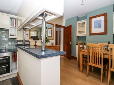 A kitchen with a dining area featuring wooden chairs and a table a countertop with metal poles light blue tiled backsplash and wooden door at Lyndhurst in Ambleside