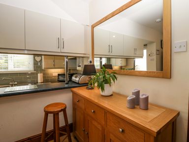 A kitchen area with white cabinets black countertop a wooden stool a wooden sideboard with three candles a potted plant and a large wooden framed mirror at Lyndhurst in Ambleside