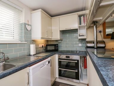 A kitchen with white cabinets a black oven a microwave a dishwasher a stainless steel sink and light blue tiled walls at Lyndhurst in Ambleside
