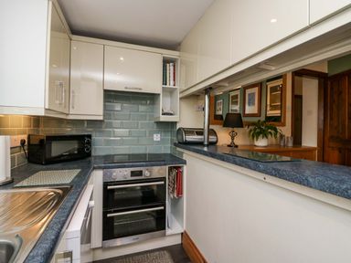 A kitchen with a sink microwave oven and toaster with blue tiled backsplash at Lyndhurst Ambleside