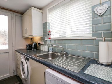 A kitchen sink with soap dispenser and paper towel holder on a countertop with blue tiled backsplash at Lyndhurst in Ambleside