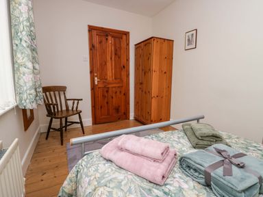 A bedroom with a wooden chair, wooden wardrobe, wooden door, and a bed with towels on a floral bedspread at Lyndhurst in Ambleside