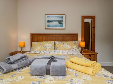 A bedroom with a wooden bed frame yellow floral bedding bedside tables with lamps and towels folded on the bed at Lyndhurst in Ambleside