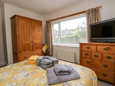 A bedroom with a wooden wardrobe a wooden chest of drawers and a bed with folded towels on a yellow floral bedspread at Lyndhurst in Ambleside