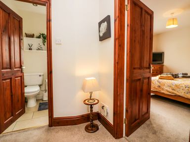 A hallway with two open wooden doors leading to a bathroom with a toilet and bedroom with a bed and TV at Lyndhurst in Ambleside