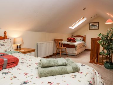 A bedroom with two single beds wooden chair bedside table lamp framed picture and potted plant at Lyndhurst Ambleside