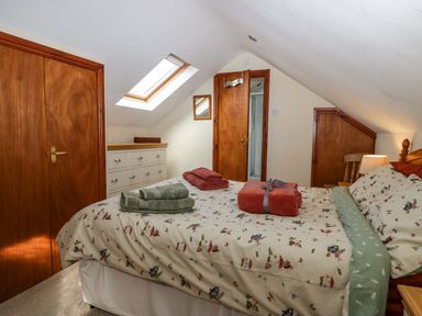 A bedroom with a bed with printed bedding green and red towels on top a chest of drawers a wooden door and a skylight window at Lyndhurst Ambleside