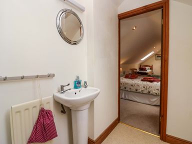 A small wash basin with hand soap and a round mirror above it in a room leading to a bedroom with two beds and towels on the beds at Lyndhurst in Ambleside