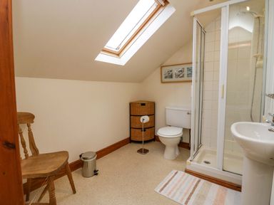 A bathroom with a toilet sink shower wooden chair waste bin and storage unit under a skylight at Lyndhurst in Ambleside