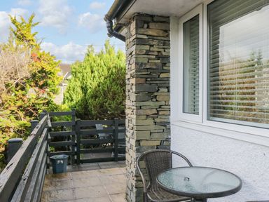 A balcony with a round glass table and chair next to a stone pillar and window at Lyndhurst Ambleside