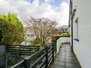 An outdoor patio area with a black railing and table with chairs next to a white building in Lyndhurst Ambleside
