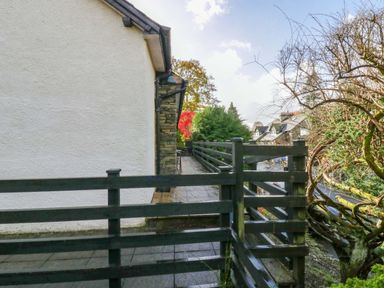 A black wooden fence and gate next to a white building with tiled walkway and trees in the background at Lyndhurst in Ambleside