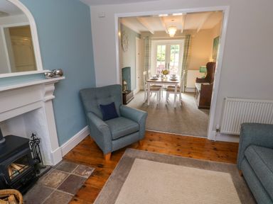 A living room with a fireplace and armchairs opening to a dining room with a table set for six at Orielton Cottage in Dinas Cross
