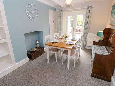 A dining room with a wooden table set for four chairs a bench a blue wall clock and French doors at Orielton Cottage in Dinas Cross