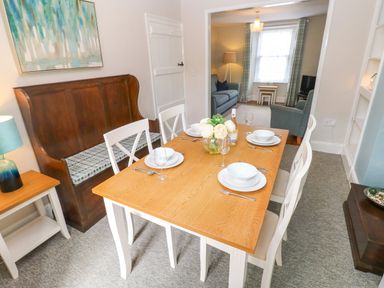 A dining room with a wooden table set for four people and a wooden bench along the wall with a painting above at Orielton Cottage in Dinas Cross