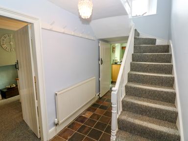 A hallway with a carpeted staircase leading up hooks on the wall radiator and open doors showing adjacent rooms at Orielton Cottage in Dinas Cross