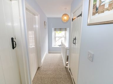 A carpeted hallway with white doors and a window at the end with a striped blind at Orielton Cottage in Dinas Cross