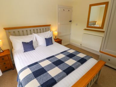 A bedroom with a bed with white sheets and blue checkered blanket bedside tables lamps a mirror radiator and a door at Orielton Cottage in Dinas Cross