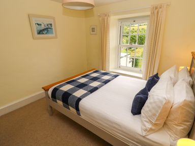 A bedroom with a bed set with pillows and a checkered blanket next to a window with curtains at Orielton Cottage in Dinas Cross