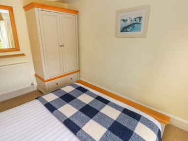 A bedroom with a bed with a blue and white checkered blanket a wardrobe a wall-mounted painting and a mirror at Orielton Cottage in Dinas Cross