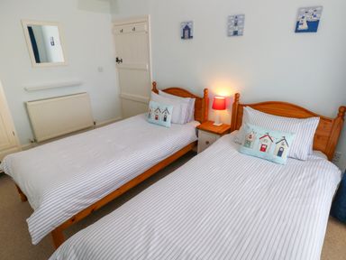 A bedroom with two single wooden beds a bedside table with a lamp and small paintings on the wall at Orielton Cottage in Dinas Cross