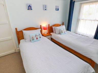 A bedroom with two single beds a nightstand with a lamp and a window with curtains at Orielton Cottage in Dinas Cross