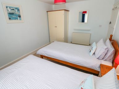 A bedroom with two single beds a wooden wardrobe a radiator a framed picture and a mirror at Orielton Cottage in Dinas Cross