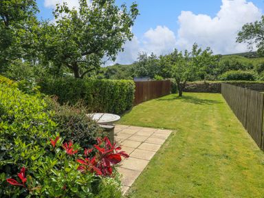 A garden with a paved patio area a round table bushes and trees with wooden fences on the sides at Orielton Cottage in Dinas Cross