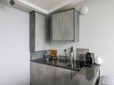 A small kitchen with grey cabinets a black countertop a sink a faucet knives a cutting board a coffee machine and a white light on the counter at Sunriser in Tara Hill near Ballymoney County Wexford